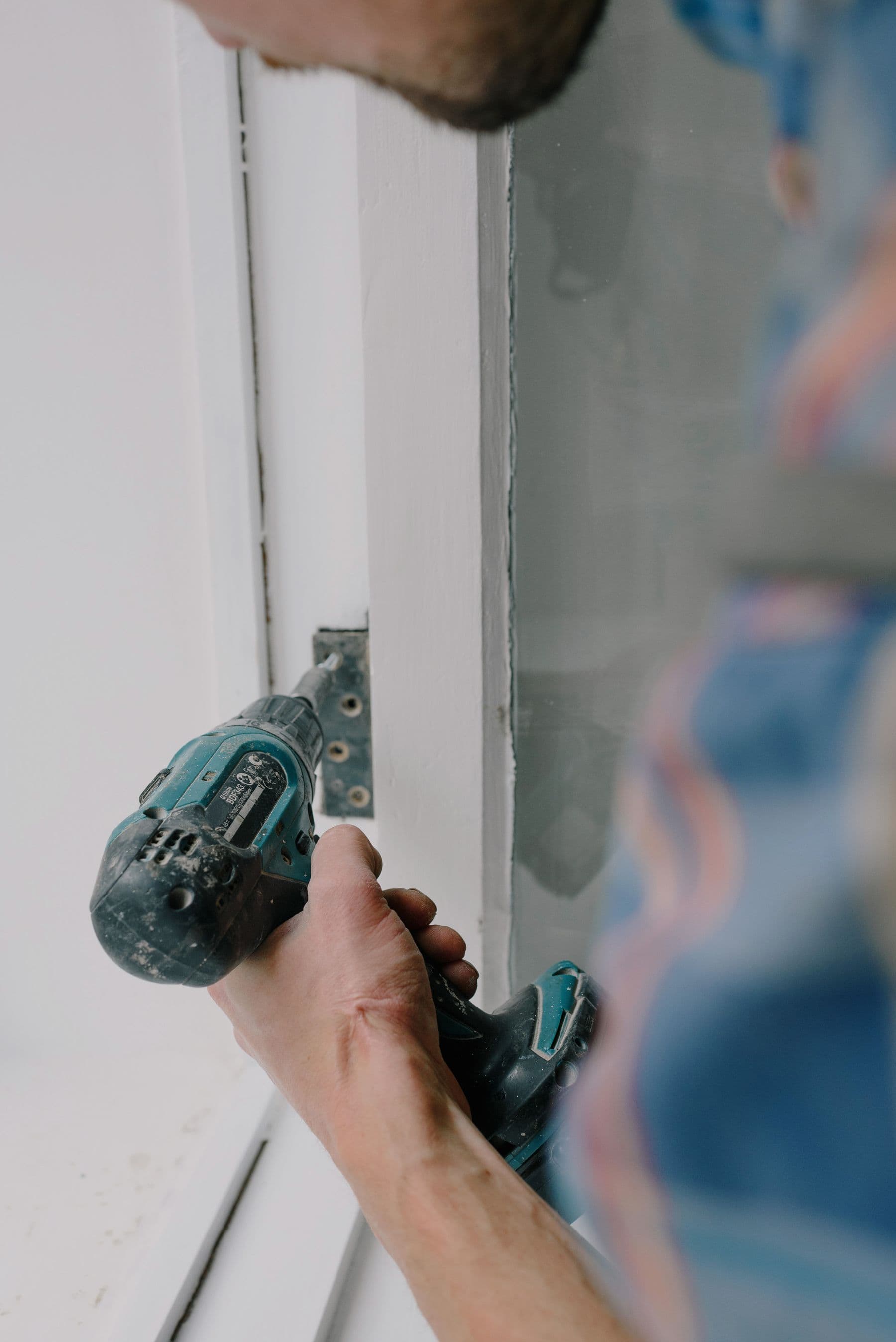 Screwdriver tightening a door hinge on a timber door