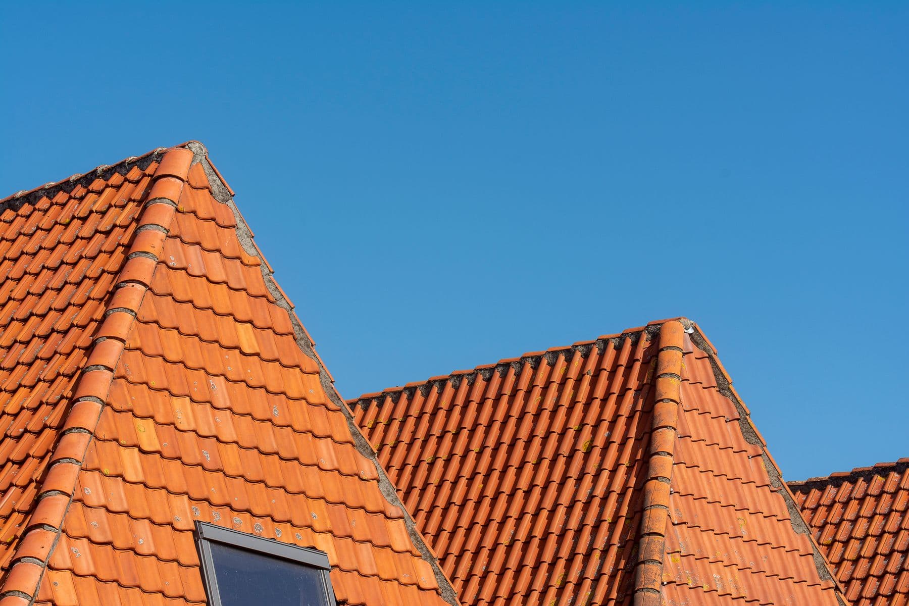 Two tiled roof ridges meeting against a clear blue sky